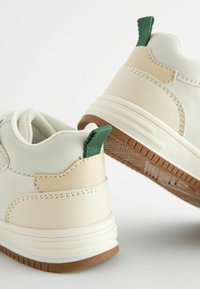 Hvide og creme sneakers med beige accenter, struktureret gummisål, grøn flap på hælen og syninger. Bagfra ses designelementerne.