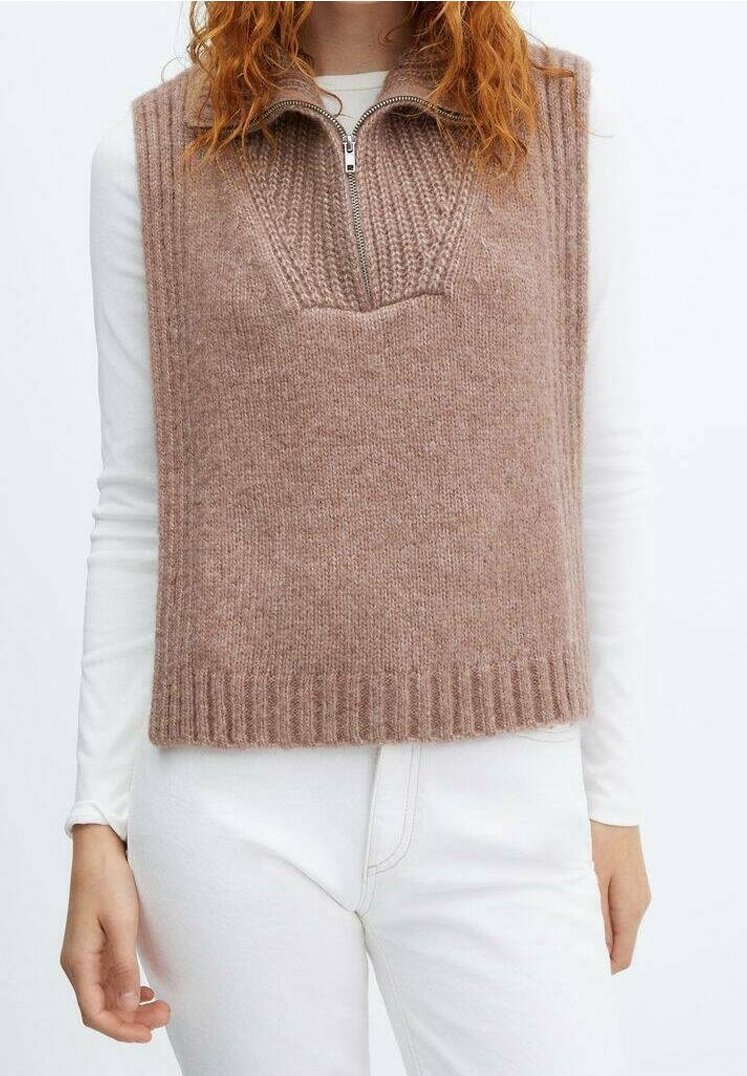 Strickweste in sanftem Beige mit hohem Kragen und Reißverschluss vorne. Mit geripptem Saum und strukturierten Mustern auf der Vorderseite. Über einem weißen Oberteil getragen.