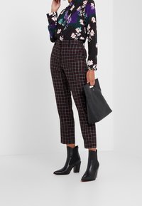 Zwart bloesje met bloemenpatroon, hooggetailleerde geruite rode en zwarte broek, zwarte enkellaarsjes met hak en een zwarte clutch.