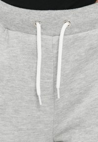 Grå joggebukser med teksturert stoff, med hvite snorer og sølvfargede metallringer, og en elastisk midje for justerbar passform.