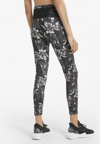 Legginsy w kwiatowy wzór, z wysokim stanem, w czarno-białym kolorze, charakteryzujące się dopasowanym krojem i gładkim, elastycznym materiałem. Połączone z czarnymi butami sportowymi.