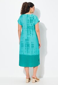 Türkises Midi-Kleid mit kurzen Ärmeln, das ein Batikmuster aufweist, das in einen einfarbigen Saum übergeht. Hergestellt aus einem leichten Stoff. Mit seitlichen Schlitzen und lockerer Passform.