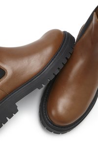 Brown leather boots with a smooth finish, black rubber sole, and elastic side panels. Features durable tread and rounded shape.