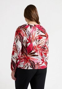 Blusa a maniche lunghe con motivo floreale in rosso, rosa e nero su sfondo bianco. Tessuto morbido, vestibilità comoda e polsini a sbuffo.