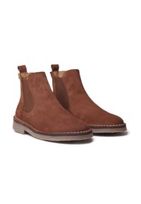 Par de botas Chelsea de ante marrón con paneles laterales elásticos y lengüetas en suelas de goma beige sobre un fondo blanco.