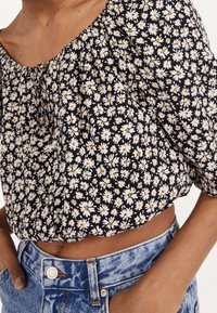 Top corto nero a fiori con margherite bianche e centri gialli. Collo arricciato e maniche corte, abbinato a jeans in denim a vita alta.