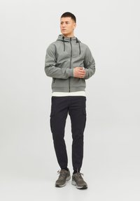 Grå zip-up hoodie med snörning i huvan, ribbade ärmar och vit foder. Kombinerad med svarta cargobyxor och grå sneakers.