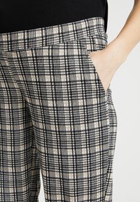 Rutig byxor i ljusbeige, svart och vit färg. Har sidofickor, en mjuk textur och en rak bendesign.