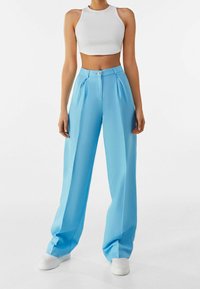 Light blue wide-leg trousers made of smooth fabric, featuring front pleats and a button closure. Paired with a white cropped tank top.