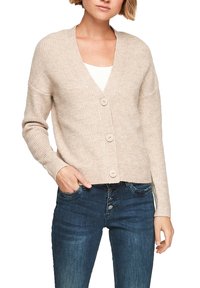 Beige ribbel cardigan met een V-hals, knopen aan de voorkant en lange mouwen, gedragen over een witte top, gecombineerd met donkerdenim jeans.