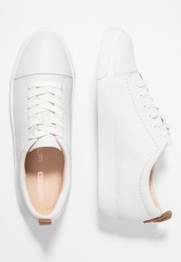 Valkoiset nahkakengät, joissa on sileä pinta, pyöreä kärki, nauhasiirtyminen ja kontrastiväriset vaaleanruskeat yksityiskohdat kantapäässä ja sisävuorissa.