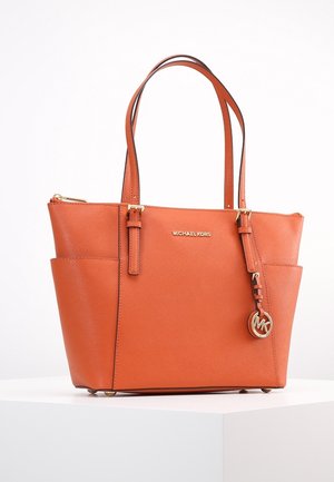 Orange Michael Kors læder tote taske med dobbelte håndtag, sidelommer, guldfarvet logo vedhæng og lynlåslukning øverst på hvid overflade.