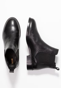 Czarne skórzane botki z elastycznymi panelami po bokach, zaokrąglonym noskiem i niskim obcasem typu słupek. Posiadają pętelkę z tyłu ułatwiającą zakładanie.