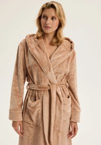 Flauszowy szlafrok w jasnobeżowym kolorze, z kapturem, paskiem do wiązania i naszywanymi kieszeniami. Miękka faktura z gładkim wykończeniem i subtelnymi akcentami designu.