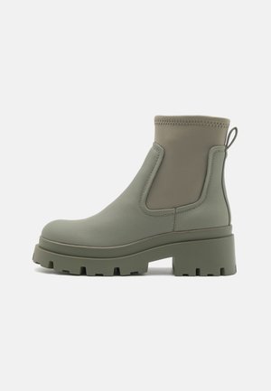 Bottines vertes en matériau synthétique texturé avec une semelle épaisse et rainurée, et des panneaux latéraux en élastique. Comprend une languette à l'arrière.