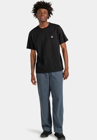 Czarna bawełniana koszulka z krótkim rękawem i małym logo na piersi, połączona z luźnymi niebieskimi spodniami i czarnymi butami.