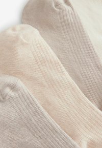 Tri parovi rebrastih čarapa u svijetloj bež, krem i mekanom taupe nijansi. Svaka čarapa ima glatku teksturu s dizajnom okruglog prsta.
