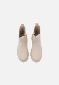 Botines beige con un upper de tela texturizada, puntera redondeada y cremallera lateral. Presenta una suela de goma resistente y una tira de tela en la parte posterior para facilitar su uso.