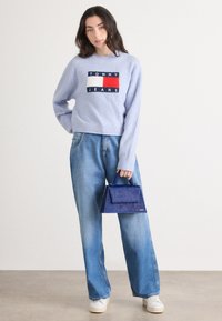 Lichtblauwe gebreide trui met ribbelmouwen, met een logo. Losvallende lichtblauwe jeans en een donkerblauwe gestructureerde handtas met een handvat.