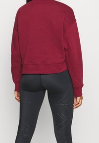 Felpa cropped color bordeaux con spalle scese, abbinata a leggings neri a vita alta caratterizzati da motivi geometrici puntinati sui lati.