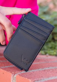 Black card holder made of smooth material with multiple card slots, a zippered compartment, and stitched detailing. Logo embossed on the front.