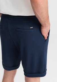 Námořnické tkané šortky se zahnuteými lemy, dvěma zadními kapsami a malým kovovým logem. Hladká textura a přizpůsobený design.