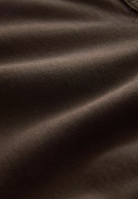 Tessuto marrone scuro con una superficie liscia e un sottile motivo a trama diagonale, che mostra onde e pieghe delicate.