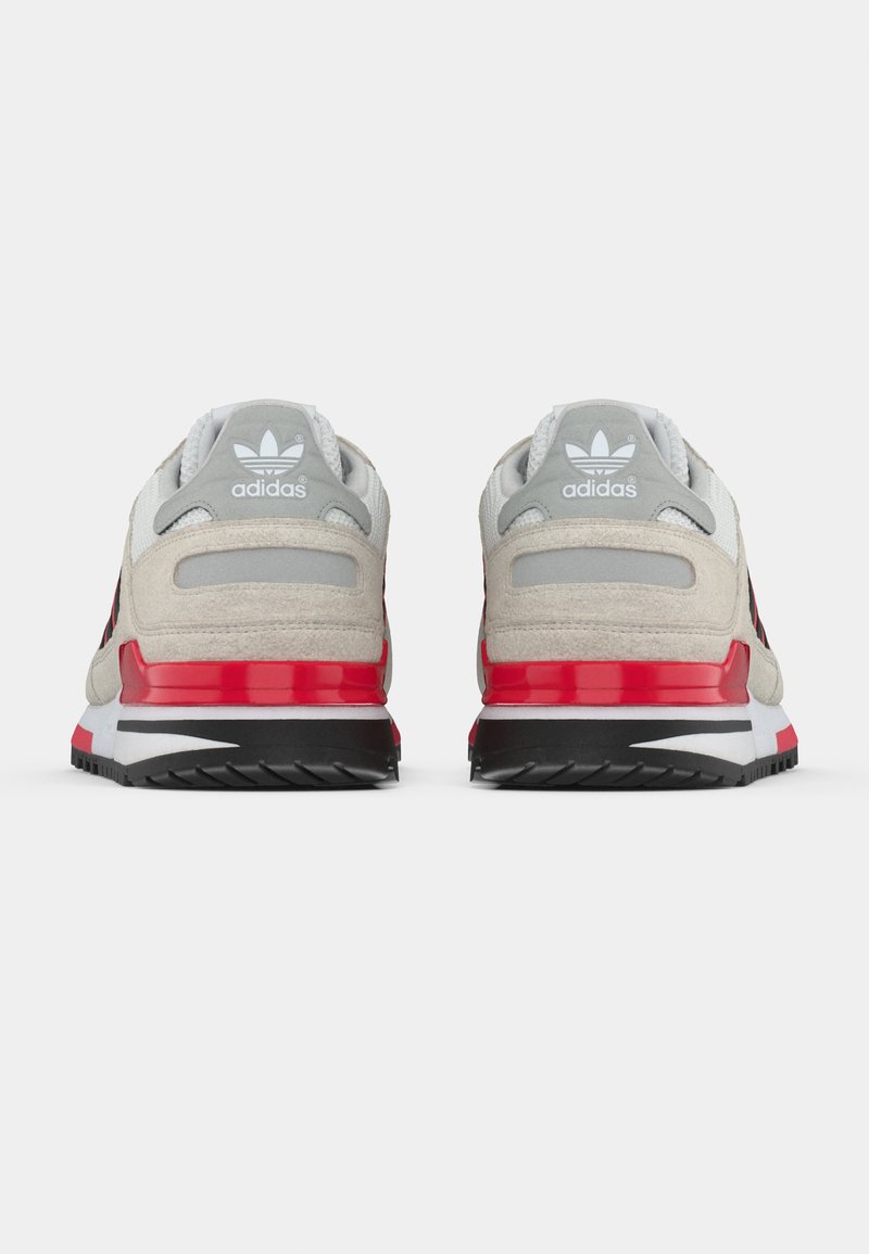 Paar beige-graue und rote Adidas-Sneaker, von hinten gezeigt, mit hervorgehobener Logo- und schwarzer Sohlen-Detail.