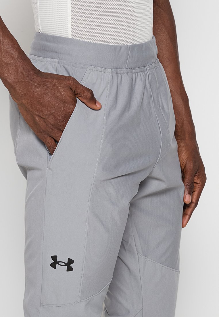 Pantalons de sport gris clair avec une taille élastique, des poches latérales, un design fuselé et un logo de marque noir sur la jambe inférieure.