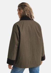 Olive green jacket with a brown corduroy collar, loose fit, and button details on sleeves. Smooth texture and plain design.
