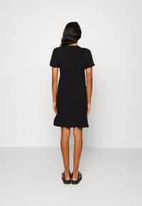 Veste preta com mangas curtas em forma de balão, corpete ajustado e bainha com pregas. Feita de tecido texturizado. Modelo a usar sandálias pretas planas.
