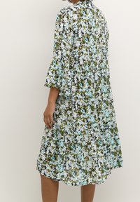 Robe florale avec des manches cloche trois-quarts. Présente un motif en bleu, vert et blanc. Silhouette fluide et longueur au genou.