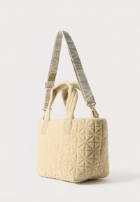 Cremefarvet quilted tote bag med to håndtag og en mønstret justerbar strap. Tekstureret stof og læderdetaljer er synlige.