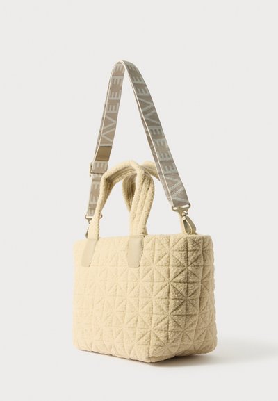 Sac cabas matelassé de couleur crème avec deux poignées et une bandoulière ajustable à motifs. Le tissu texturé et les accents en cuir sont visibles.