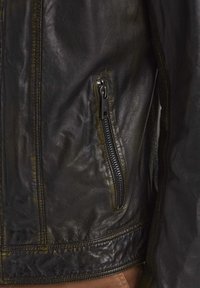 Schwarze Lederjacke mit einer Reißverschlusstasche, strukturiertem Finish und Kontrastnähten entlang dem Saum und den Nähten.