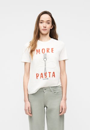 Giovane donna con capelli lunghi che indossa una maglietta bianca con la scritta "MORE PASTA PLEASE" accompagnata da un disegno di forchetta e pasta, abbinata a pantaloni verde chiaro.