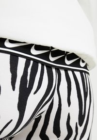 Black and white zebra print leggings with a branded elastic waistband featuring repeated Nike logos. Soft, stretchy fabric and snug fit.