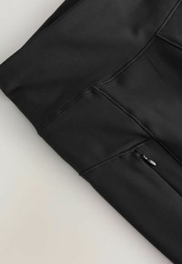 Sorte atletiske leggings med synlige sømme og en lille lynlåslomme på den øverste lårdel.