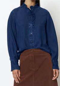 Navy knoop blouse met een gerimpelde kraag en een voorpaneel, gecombineerd met een bruine rok. De blouse heeft lange mouwen en een ontspannen pasvorm.