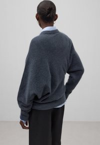 Donkergrijze oversized trui met afgezakte schouders, geribbelde zoom en een zachte textuur, gedragen over een lichtblauw overhemd met kraag.