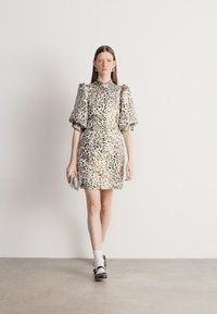 Sukienka w panterkę z krótkimi bufkami, dopasowaną sylwetką i wysokim dekoltem. Gładka tkanina o delikatnym połysku; długość do kolan.