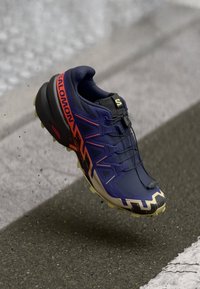 Salomon running shoe, navy upper, orange accents, textured sole, lightweight design, and a quick lace system. Notable tread pattern.