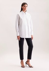 White and navy striped long-sleeve shirt with a button-up collar, paired with black slim-fit pants and strappy black heels.