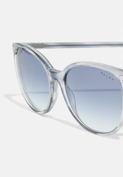 Ochelari de soare cu formă cat-eye, transparenți, cu lentile gradient în nuanțe de albastru, având un ramă groasă și cuvântul "RALPH" imprimat pe lentilă. Brațe texturate.