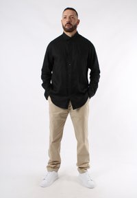 Camicia nera con bottoni, pantaloni beige e sneakers bianche. La camicia ha un colletto e maniche lunghe; i pantaloni sono a vestibilità rilassata senza motivi visibili.