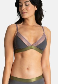 Le soutien-gorge présente un tissu gris avec une dentelle lavande en dessous, une large bande vert olive sous la poitrine, et des bretelles fines et réglables.