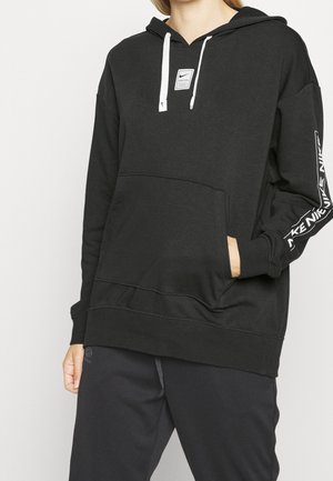 Frau trägt schwarzen Nike Pro Hoodie mit weißen Kordeln, Fronttasche und weißem Nike-Schriftzug am linken Ärmel.