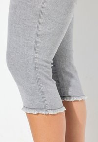 Pantalones capri de mezclilla gris con dobladillo deshilachado y diseño ajustado, que cuentan con una textura suave y un corte a la altura del tobillo.