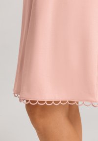 Abito rosa con una texture liscia, design fino al ginocchio e orlo ondulato con cuciture decorative nella parte inferiore.