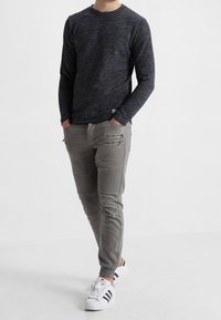 Navy strukturierter Pullover, taillierte graue Hose mit Zickzack-Stitching und Reißverschlusstaschen, kombiniert mit weißen Sneakers. Einfaches, modernes Design.